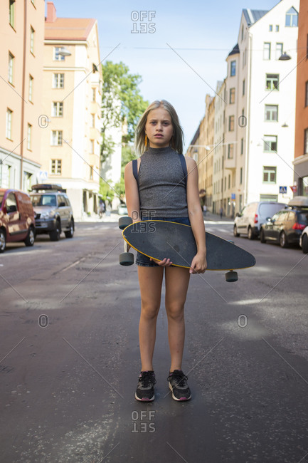 Girl standing in street, holding skateboard