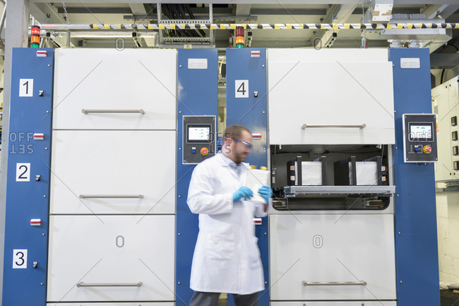 Scientist walking by lithium ion pouch cell manufacture machine in battery research facility
