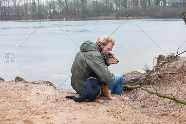 Mature man hugging dog on riverbank