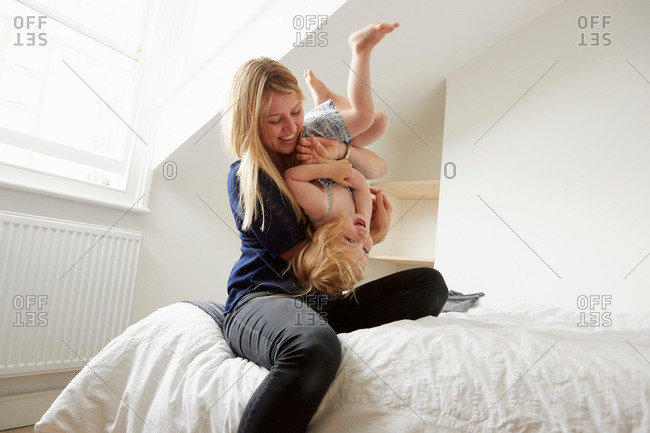Mid adult woman turning toddler daughter upside down on bed