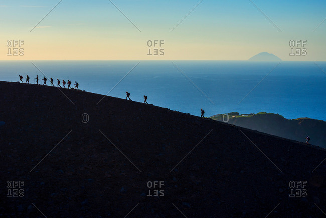 Large group of silhouetted tourists walking rim at Gran Cratere, Vulcano Island, Aeolian Islands, Sicily, Italy