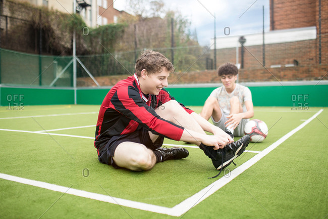 Two young men on urban soccer field, tying shoelaces