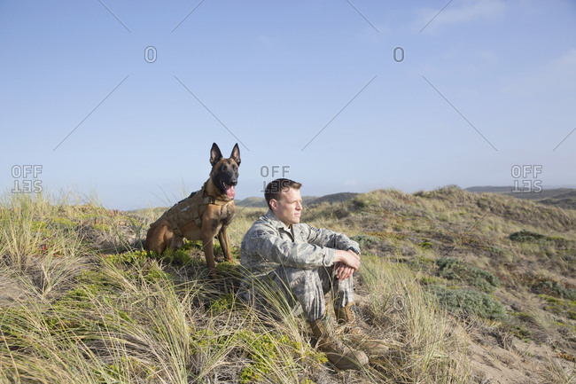 Portrait of soldier and his service dog sitting on a hillside