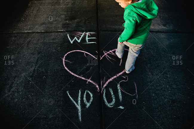 Little boy walking across a heart drawing in chalk on a sidewalk