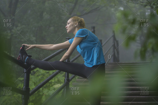 Young woman using stairs to stretch during a rainy day workout