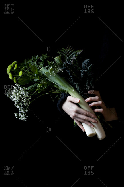 Hands holding a bouquet of vegetables and wildflowers on a black background