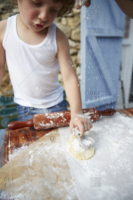 Boy standing at an outdoor table making heart-shaped cookies