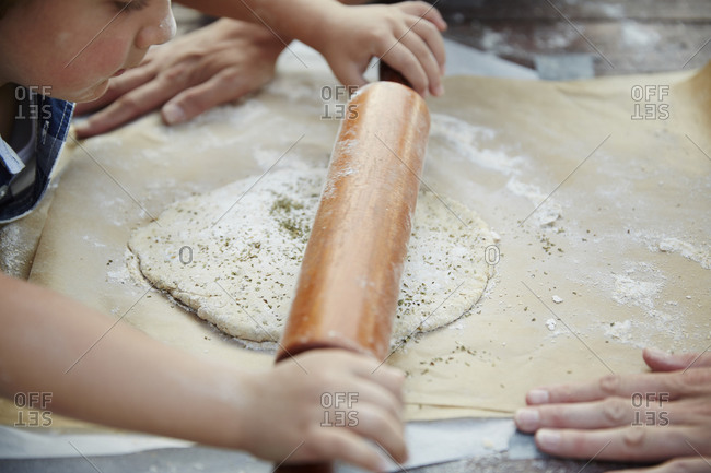 Little boy rolling dough with help at an outdoor table