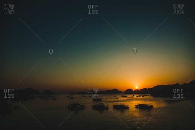 Silhouette of boats and buildings in a mountain lined harbor at sunset