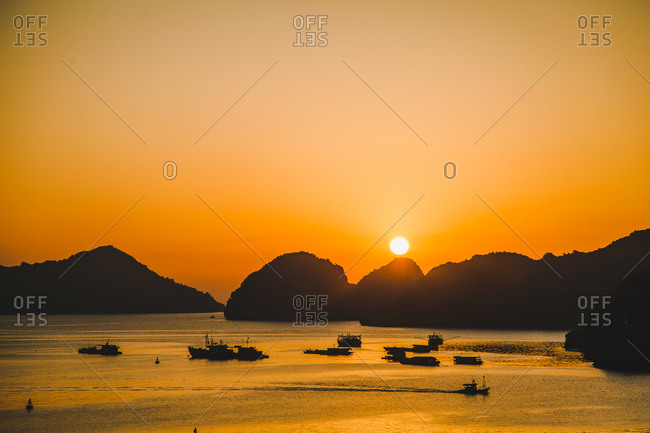 Silhouette of boats in a mountain lined harbor at sunset
