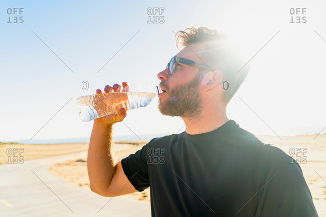Young man, by beach, drinking from water bottle