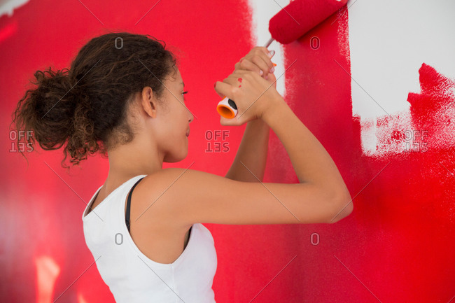 Girl painting wall red with paint roller