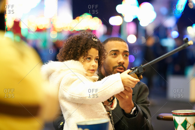 Father helping daughter with rifle at shooting gallery at funfair