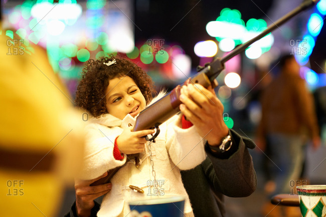 Father helping daughter with rifle at shooting gallery at a fair