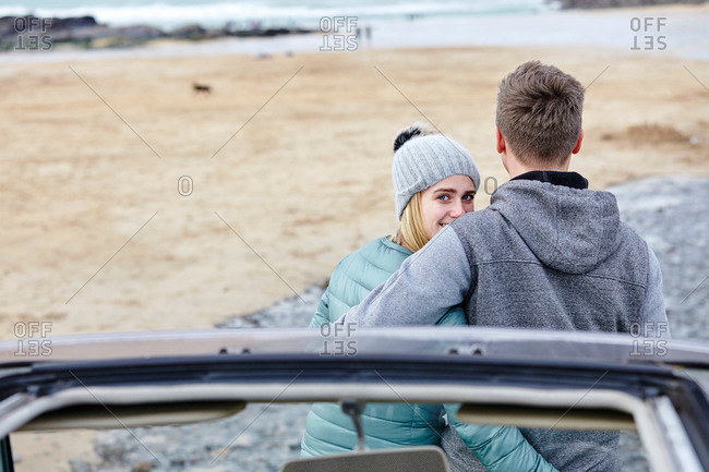 Young couple with arms around each other at beach, Constantine Bay, Cornwall, UK