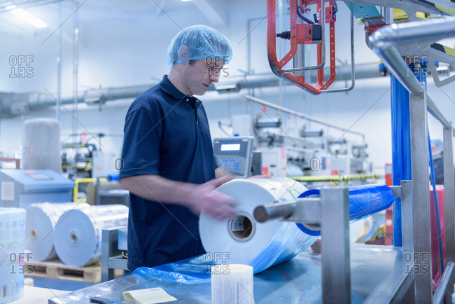 Worker moving roll of packaging in food packaging printing factory