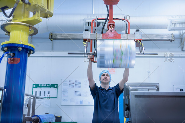 Worker lifting  roll of packaging in food packaging printing factory