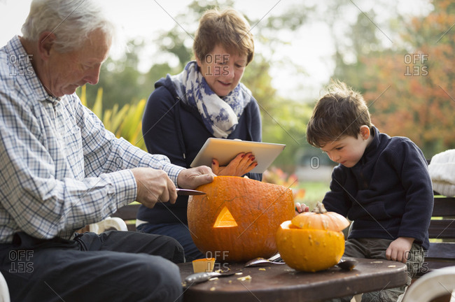 Two adults and a child with large pumpkins carving jack-o-lanterns for Halloween
