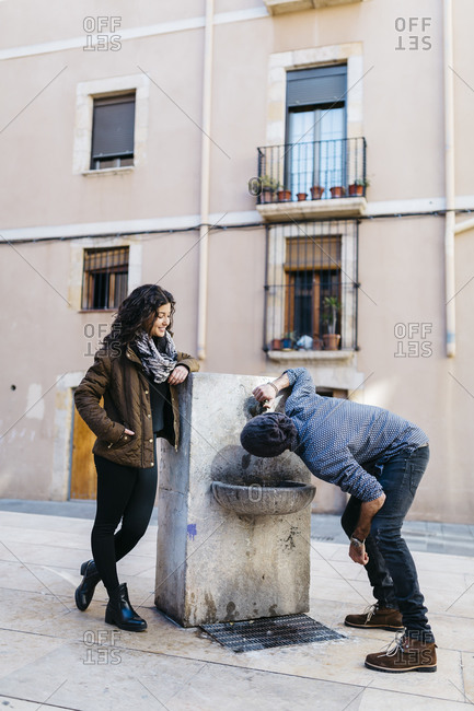 Spain, Tarragona, Young couple, man drinking from drinking fountain