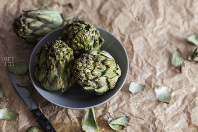 Three artichokes in a bowl on crumpled brown paper