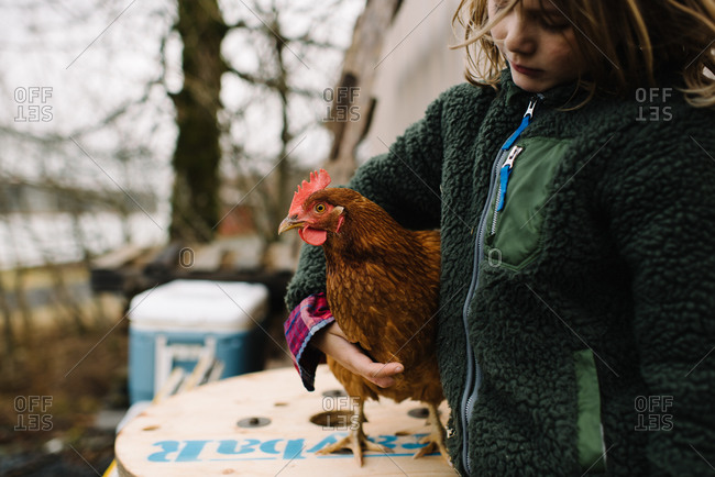 Little girl standing at a wooden spool wrapping her arm around a chicken