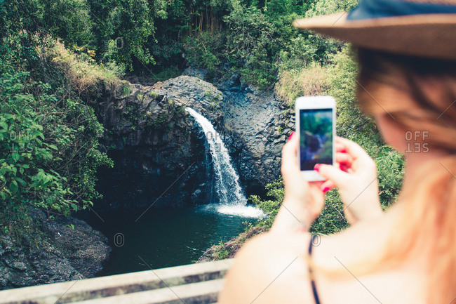 Over shoulder view of female tourist photographing waterfall on smartphone, Haleakala, Hawaii, USA