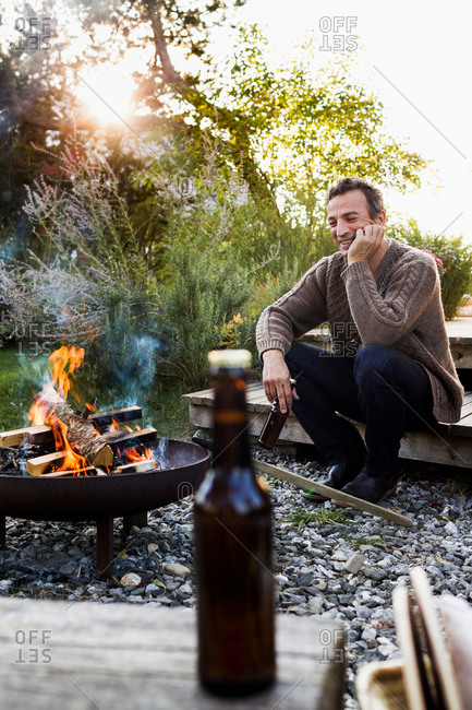 Mature man sitting by fire pit with beer, relaxing