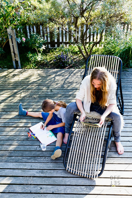 Mother using tablet, daughter drawing on wooden decking