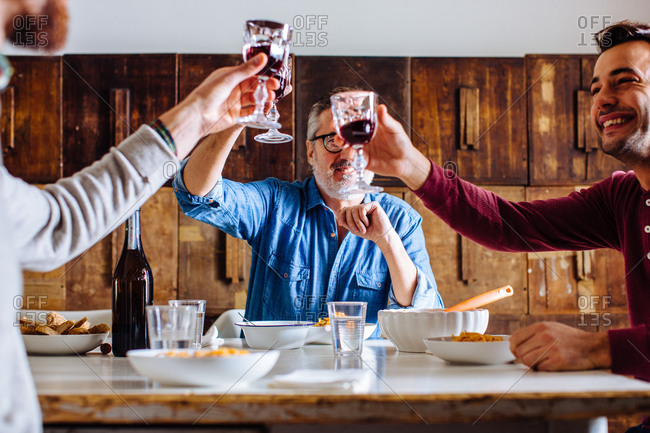 Mature man and adult sons raising a glass of red wine at dining table