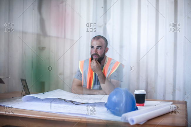 Site manager sitting at desk with blueprint in portable cabin