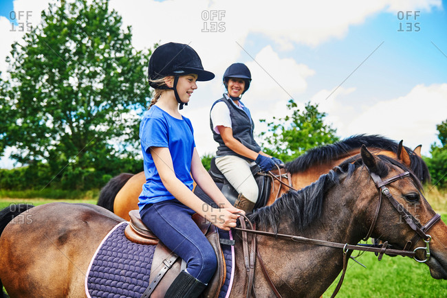 Side view of mature woman and girl on horseback wearing riding hats smiling