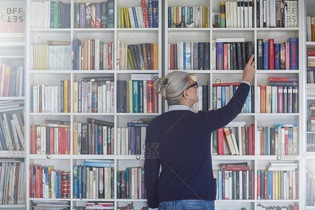 Rear view of mature woman selecting book from bookshelves
