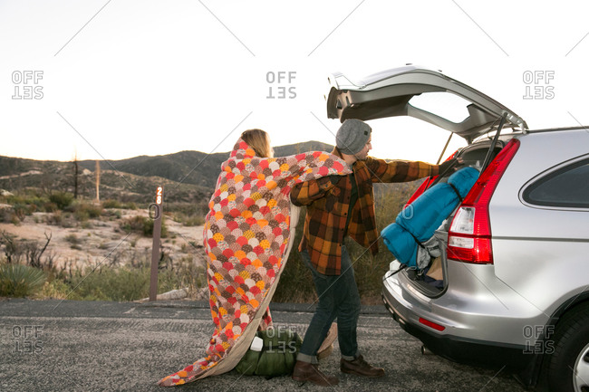 Young couple putting camping equipment in boot of car