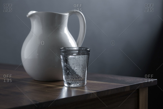 Glass of water and white water pitcher on a wood table