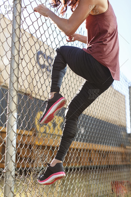 Woman wearing running shoes climbing a chain link fence
