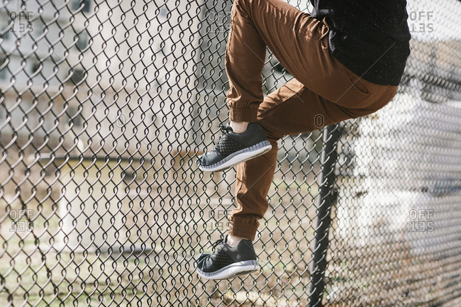 Person wearing running shoes climbing a chain link fence