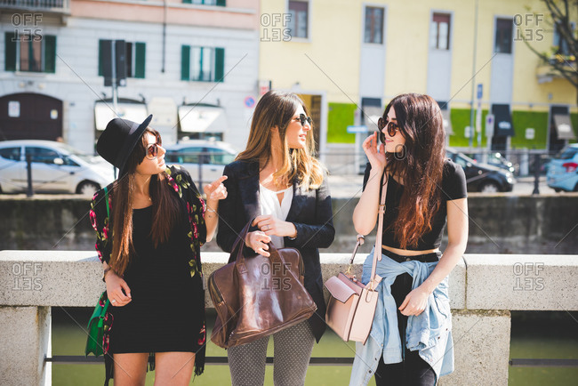 Three stylish young female friends chatting at city riverside