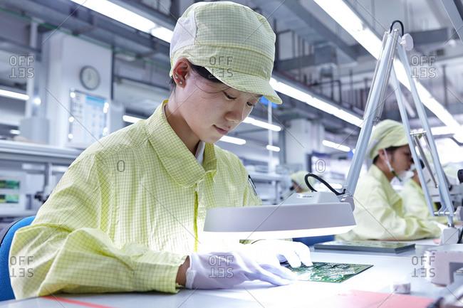 Young woman working at quality check station at factory producing flexible electronic circuit boards