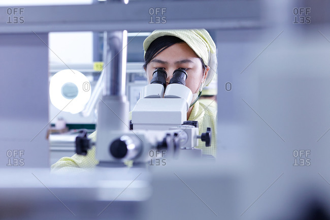 Young woman with microscope at quality check station at factory producing flexible electronic circuit boards
