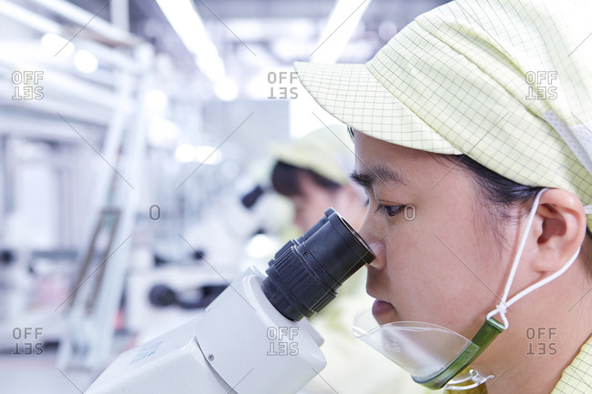 Young woman using microscope at quality check station at factory producing flexible electronic circuit boards