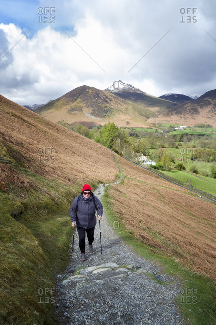 A woman walking up a path on a hillside in the Lake District with a trekking pole