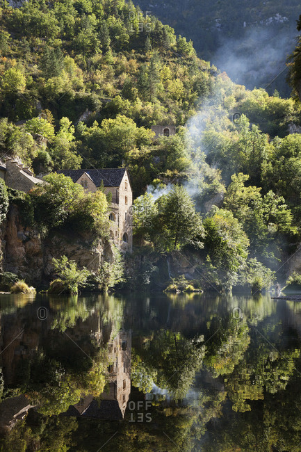 Houses on a steep hillside, reflected on the water of a river  woodland, and a thin stream of rising wood smoke