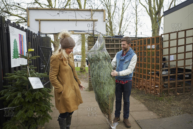 A member of staff carrying a Christmas tree talking to a woman client