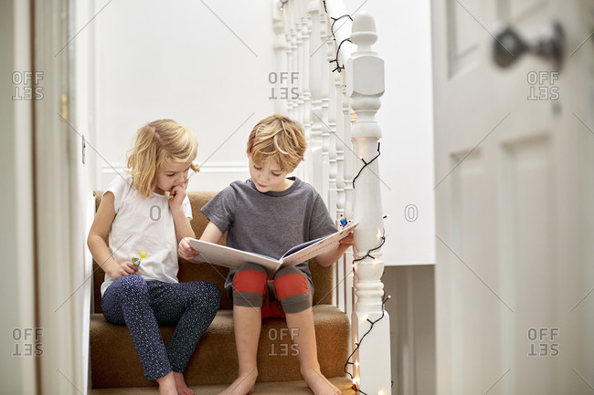 Two children seated side by side on the stairs at home, reading a book together