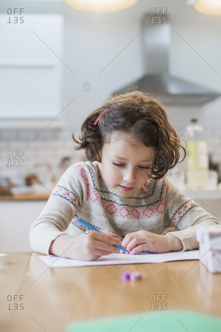 A girl sitting at a kitchen table writing a card or letter