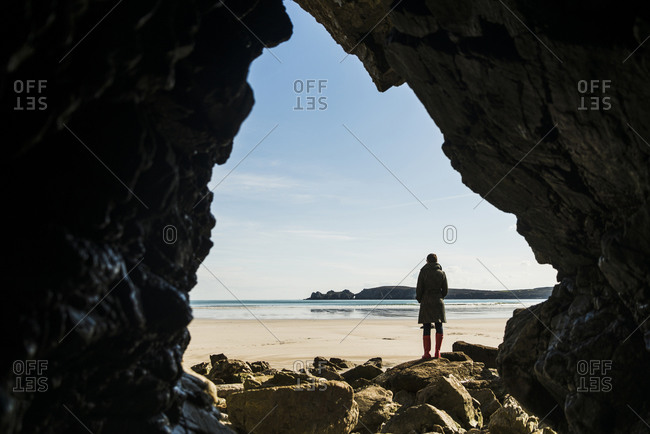 France, Bretagne, Finistere, Crozon peninsula, woman standing on the beach as seen from rock cave
