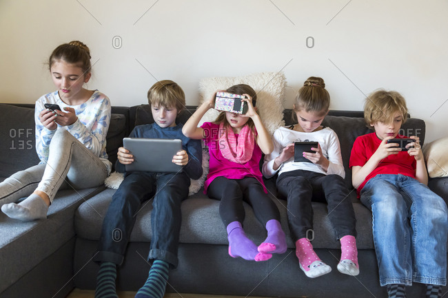 Group picture of five children sitting on one couch using different digital devices