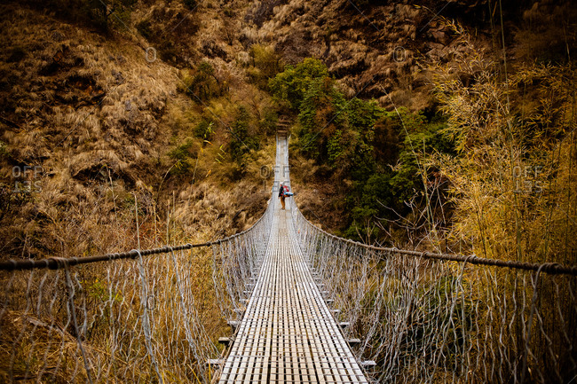 Person trekking across a narrow suspension bridge in Nepal