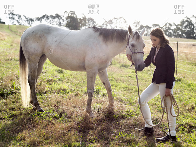 Teenage girl leading grey horse in field