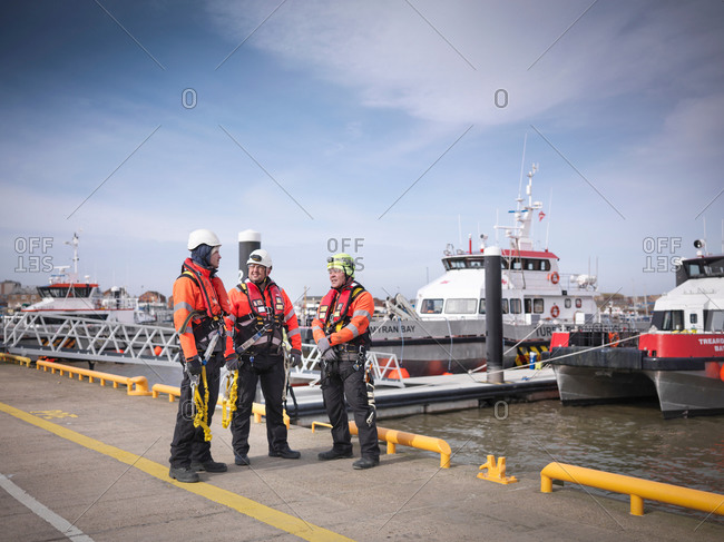 Three offshore windfarm engineers on quayside with boats in the background